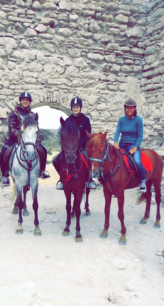 Trois voyageuses à cheval devant une ancienne porte en pierre au Maroc